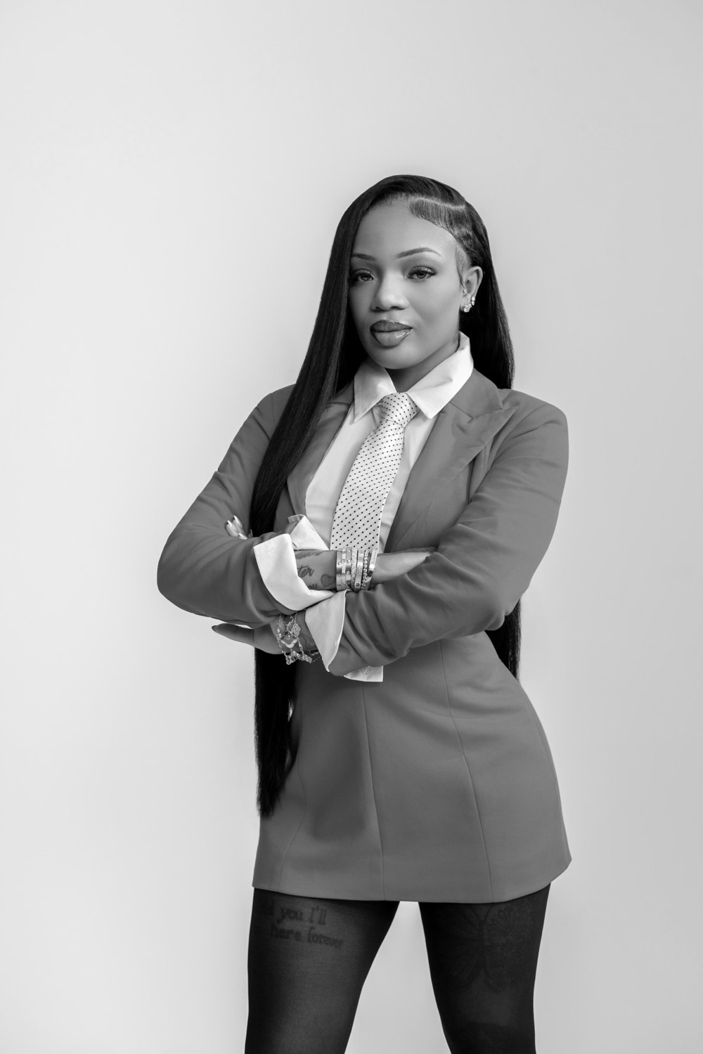 Gloria Woods standing with arms crossed in a suit and polka dot tie